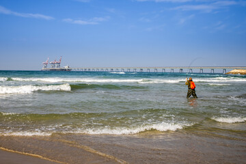 Wall Mural - A man is fishing in front of the  Power plant Orot Rabin (Rabin's Lights) on the Mediterranean coast near the city of Hadera, Israel.