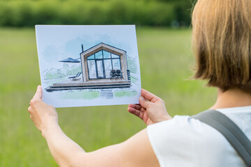 Wall Mural - Architect holding barn house  hand drawn sketch in front of a plot of land