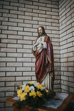 Vertical Shot Of Jesus Christ's Sculpture With Decorative Flowers In Front Of It