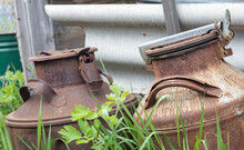 Two Old Rusty Metal Cans In The Countryside. Container For Transporting Liquids, Milk Or Liquid Fuels With Several Handles. Milk Bank Of A Cylindrical Form With A Wide Mouth. Flask With Sealed Lid.