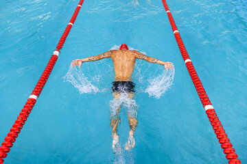 One athlete, male professional swimmer in goggles and red swimming cap swimming at public pool, at open-air. Sport, power, energy, style, hobby concept.