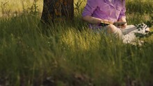 Unrecognizable Woman Reading Book, Sitting On Green Grass Near Tree In Summertime. Relaxed Secluded Faceless Female Relaxing In Nature With Book.