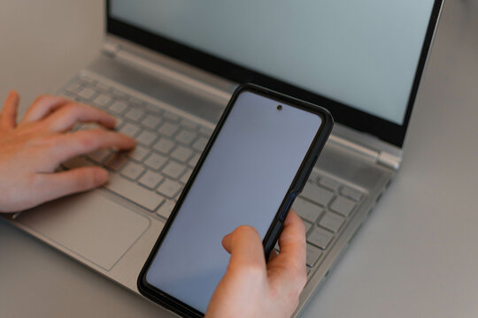 Top view mockup image of hands holding a blank white screen mobile phone with laptop computer and tablet pc on the table in office