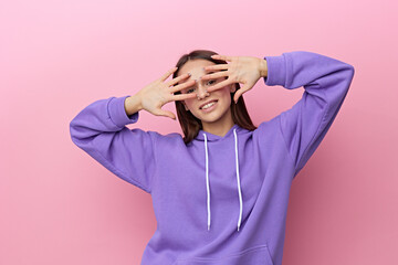 Wall Mural - a joyful, happy woman stands on a pink background in a purple tracksuit and covers her face with her hands