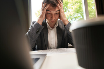 Male grabbing head in despair while looking at spreadsheet