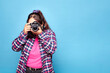 © Lux Images - Young curvy Latina woman taking a photo with a reflex camera in a studio, isolated on blue background.