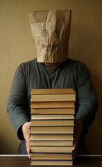 unrecognizable man with a paper bag on his head reads a book. The kraft paper bag with painted eyes and smiley mouth.