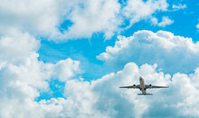 Commercial Airline Flying On Blue Sky And White Fluffy Clouds. Under View Of Airplane Flying. Passenger Plane After Take Off Or Going To Landing Flight. Vacation Travel Abroad. Air Transportation.