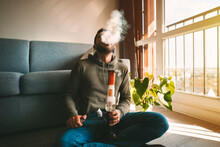 Man Smoking Bong And Exhaling The Smoke At Home. Man Smoking Pot, Medical Marijuana Or Cannabis From A Bong Or Water Pipe. Cannabis And Weed Legalisation Concept