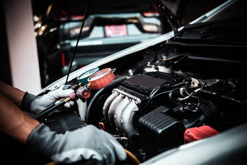 Hand of auto mechanic using measuring manifold gauge check the refrigerant and filling car air conditioner for fix and checking for heat repair service or support maintenance and car insurance.