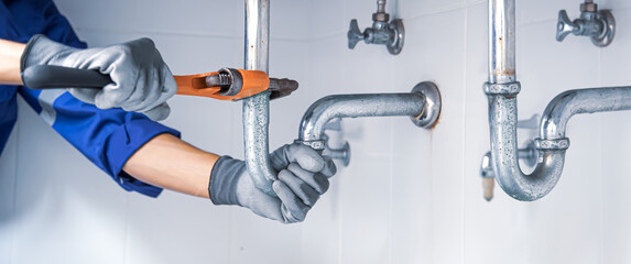 Technician plumber using a wrench to repair a water pipe under the sink. Concept of maintenance, fix water plumbing leaks, replace the kitchen sink drain, cleaning clogged pipes is dirty or rusty.