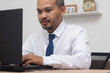 © vachiravit - A happy man with a tie smiles while working on his laptop.