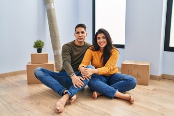 Canvas Print - Young couple sitting on the floor at new home smiling looking to the side and staring away thinking.