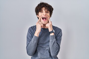 Sticker - Young man standing over isolated background smiling with open mouth, fingers pointing and forcing cheerful smile