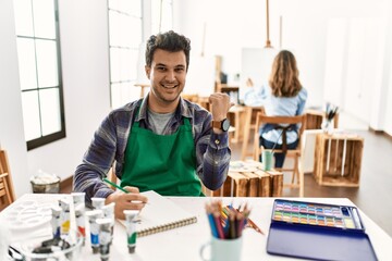 Poster - Young artist man at art studio pointing to the back behind with hand and thumbs up, smiling confident