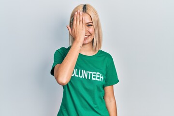 Poster - Beautiful blonde woman wearing volunteer t shirt covering one eye with hand, confident smile on face and surprise emotion.