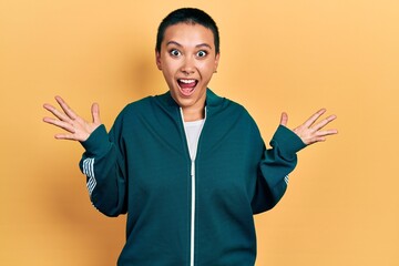 Poster - Beautiful hispanic woman with short hair wearing sporty jacket celebrating crazy and amazed for success with arms raised and open eyes screaming excited. winner concept