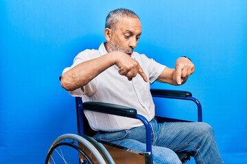 Canvas Print - Handsome senior man with beard sitting on wheelchair pointing down with fingers showing advertisement, surprised face and open mouth