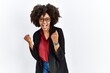 © Krakenimages.com - African american woman with afro hair wearing business jacket and glasses very happy and excited doing winner gesture with arms raised, smiling and screaming for success. celebration concept.