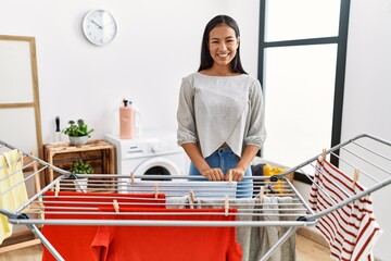 Poster - Young hispanic woman putting fresh laundry on clothesline with a happy and cool smile on face. lucky person.