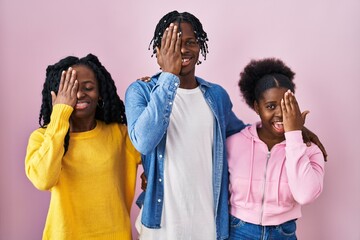 Poster - Group of three young black people standing together over pink background covering one eye with hand, confident smile on face and surprise emotion.