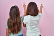 © Krakenimages.com - Young mother and daughter standing over pink background posing backwards pointing ahead with finger hand