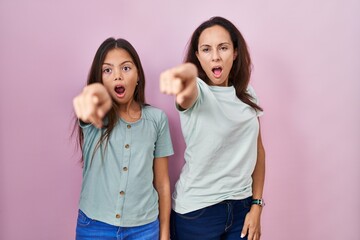 Wall Mural - Young mother and daughter standing over pink background pointing with finger surprised ahead, open mouth amazed expression, something on the front