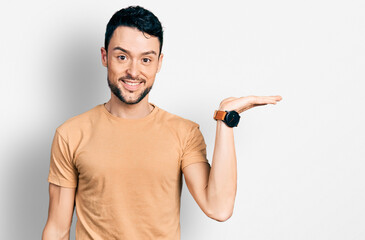 Poster - Hispanic man with beard wearing casual t shirt smiling cheerful presenting and pointing with palm of hand looking at the camera.