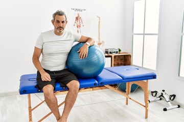 Canvas Print - Middle age hispanic man at pain recovery clinic holding pilates ball skeptic and nervous, frowning upset because of problem. negative person.