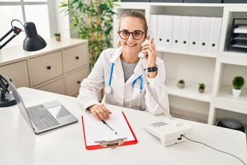 Canvas Print - Young doctor woman speaking on the phone looking positive and happy standing and smiling with a confident smile showing teeth