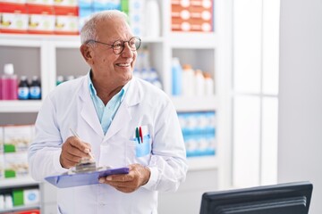 Canvas Print - Senior grey-haired man pharmacist writing on document at pharmacy