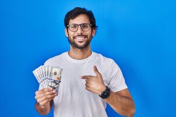 Poster - Handsome latin man holding dollars banknotes pointing finger to one self smiling happy and proud