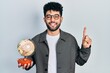 © Krakenimages.com - Young arab man with beard holding vintage world ball smiling with an idea or question pointing finger with happy face, number one