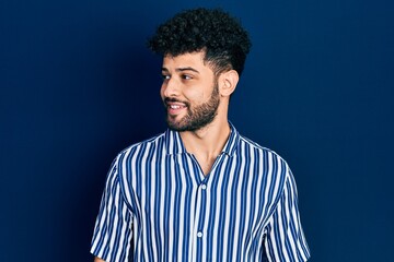 Sticker - Young arab man with beard wearing casual striped shirt looking to side, relax profile pose with natural face and confident smile.