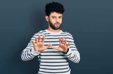 Poster - Young arab man with beard wearing casual striped sweater moving away hands palms showing refusal and denial with afraid and disgusting expression. stop and forbidden.