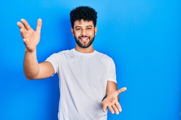 Sticker - Young arab man with beard wearing casual white t shirt smiling cheerful offering hands giving assistance and acceptance.