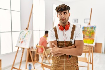 Poster - Young hispanic man at art studio smiling looking to the side and staring away thinking.