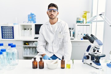 Poster - Young hispanic man working at scientist laboratory thinking attitude and sober expression looking self confident