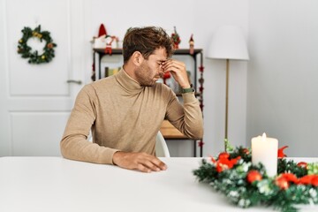 Sticker - Young handsome man with beard sitting on the table by christmas decoration tired rubbing nose and eyes feeling fatigue and headache. stress and frustration concept.