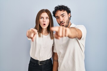 Wall Mural - Young couple wearing casual clothes standing together pointing with finger surprised ahead, open mouth amazed expression, something on the front