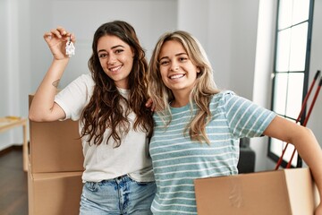 Canvas Print - Young beautiful couple smiling happy holding cardboard box and key of new home.