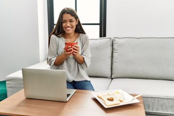 Sticker - Young latin woman having breakfast working sitting on sofa at home