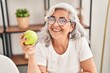 Leinwandbild Motiv Middle age woman smiling confident holding apple at home