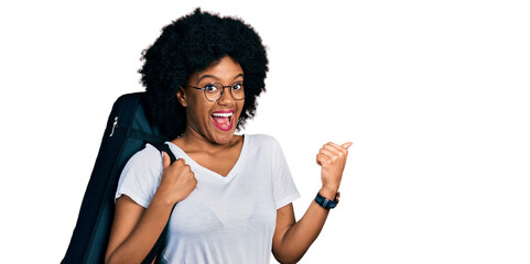 Poster - Young african american woman wearing guitar case pointing thumb up to the side smiling happy with open mouth