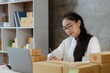© kamiphotos - A beautiful Asian business owner opens an online store, she is checking orders from customers, sending goods through a courier company, concept of a woman opening an online business.