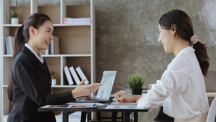 Wall Mural - Atmosphere in the office of a startup company, two female employees are discussing, brainstorming ideas to working on summaries and marketing plans to increase sales and prepare reports to managers.