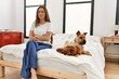 © Krakenimages.com - Young brunette woman sitting on the bed with two dogs skeptic and nervous, disapproving expression on face with crossed arms. negative person.