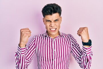 Wall Mural - Young hispanic man wearing casual clothes angry and mad raising fists frustrated and furious while shouting with anger. rage and aggressive concept.