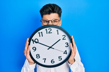 Canvas Print - Young hispanic man holding big clock over face clueless and confused expression. doubt concept.