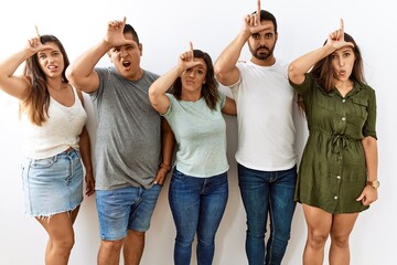 Sticker - Group of young hispanic friends standing together over isolated background making fun of people with fingers on forehead doing loser gesture mocking and insulting.